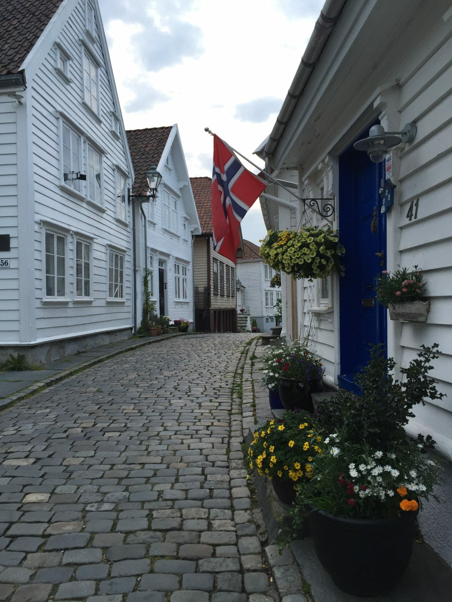 A cobblestone street with whitewashed houses some plants and a Norwegian flag in the city of Stavanger, Norway