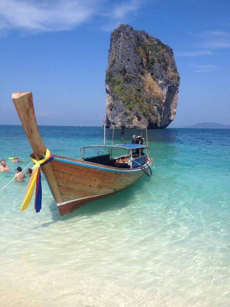 A traditional Thai boat on the crystal-clear of Poda Island, Thailand, and a limestone rock in the backdrop
