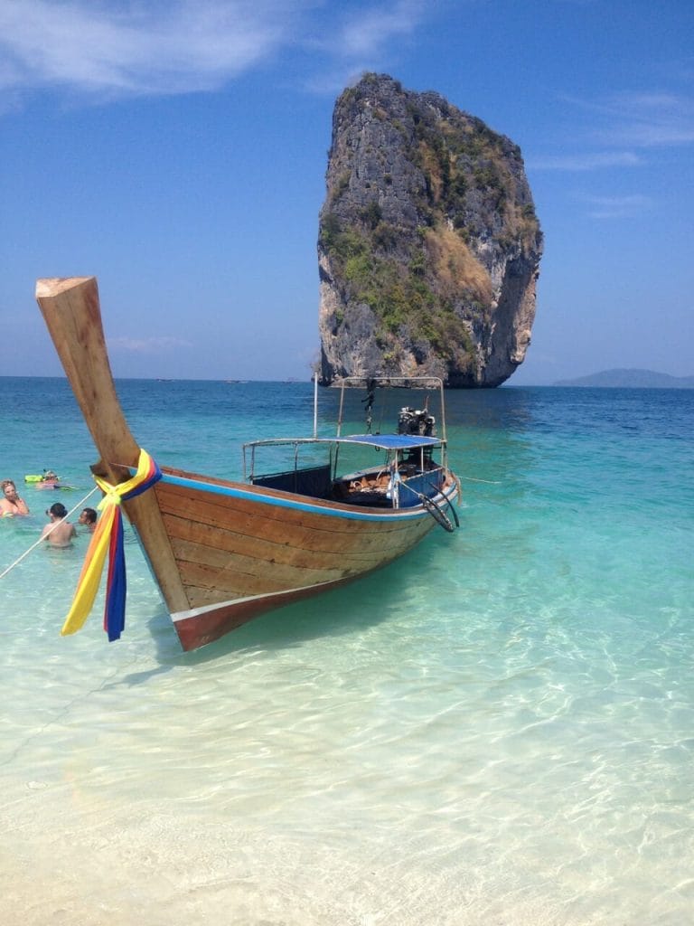 A traditional Thai boat on the crystal-clear of Poda Island, Thailand, and a limestone rock in the backdrop