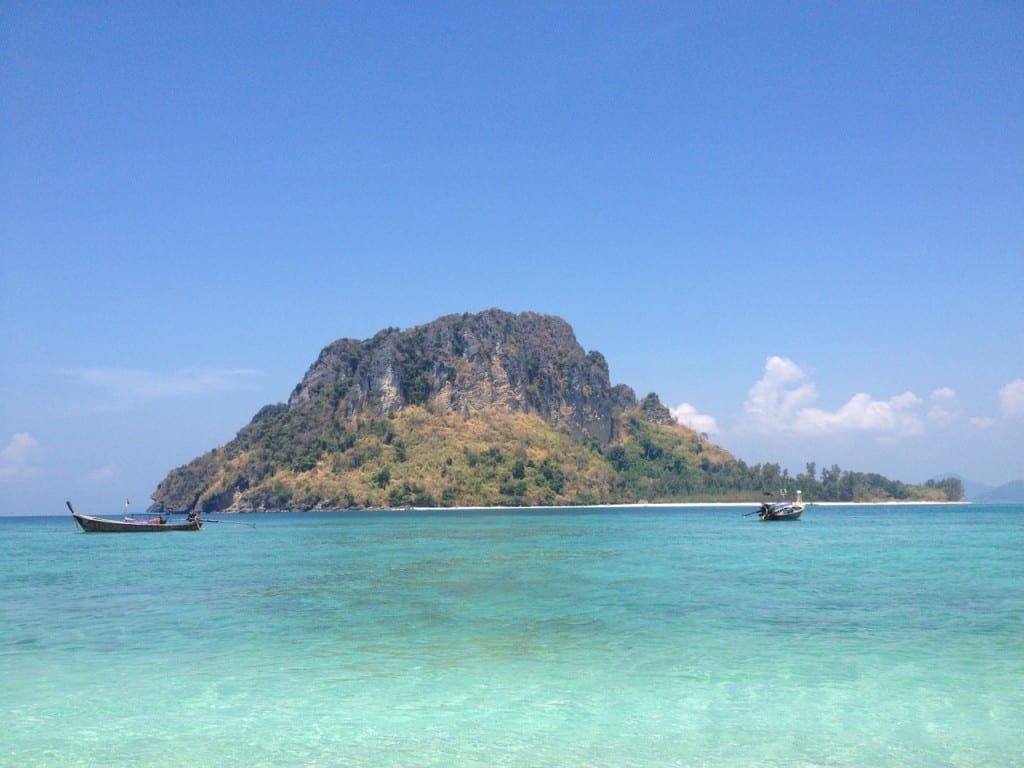 Two traditional Thai boat sailings on the crystalline turquoise water of Tup Island, Thailand, and a limestone mountain in the background partially covered by vegetation