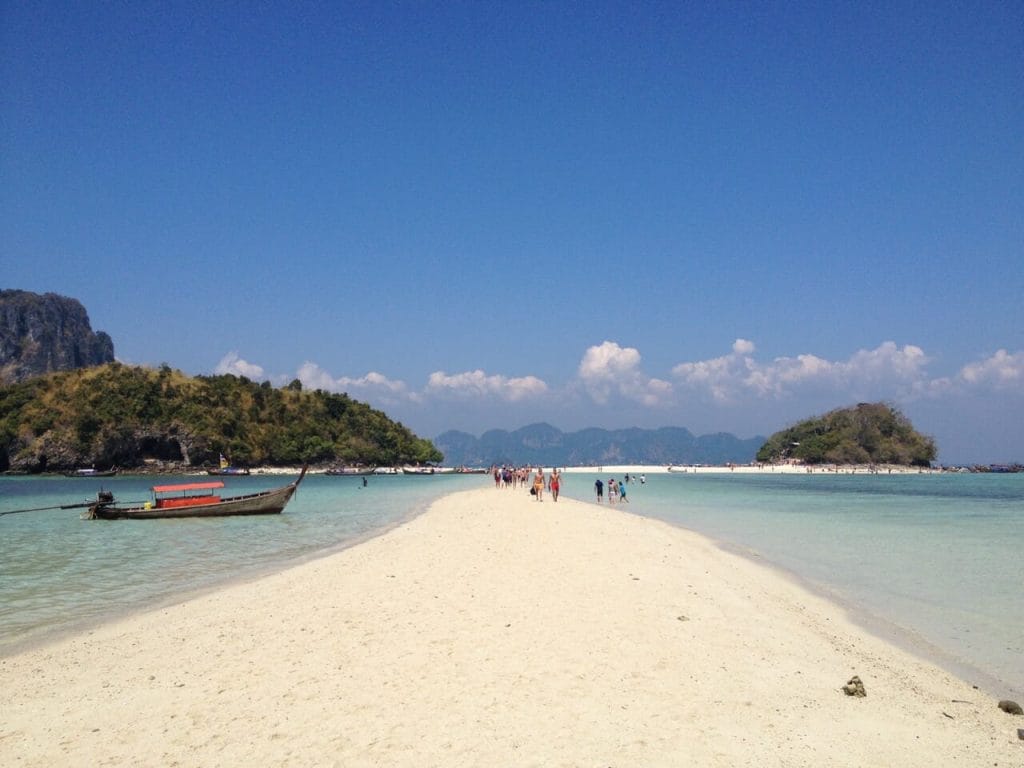 People walking on a sandbank on Tup Island, Thailand, surrounded by crystal-clear turquoise water.