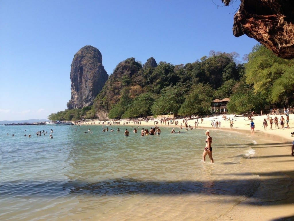 People walking on Phra Nang Beach and limestone mountains covered with vegetation in the backdrop 