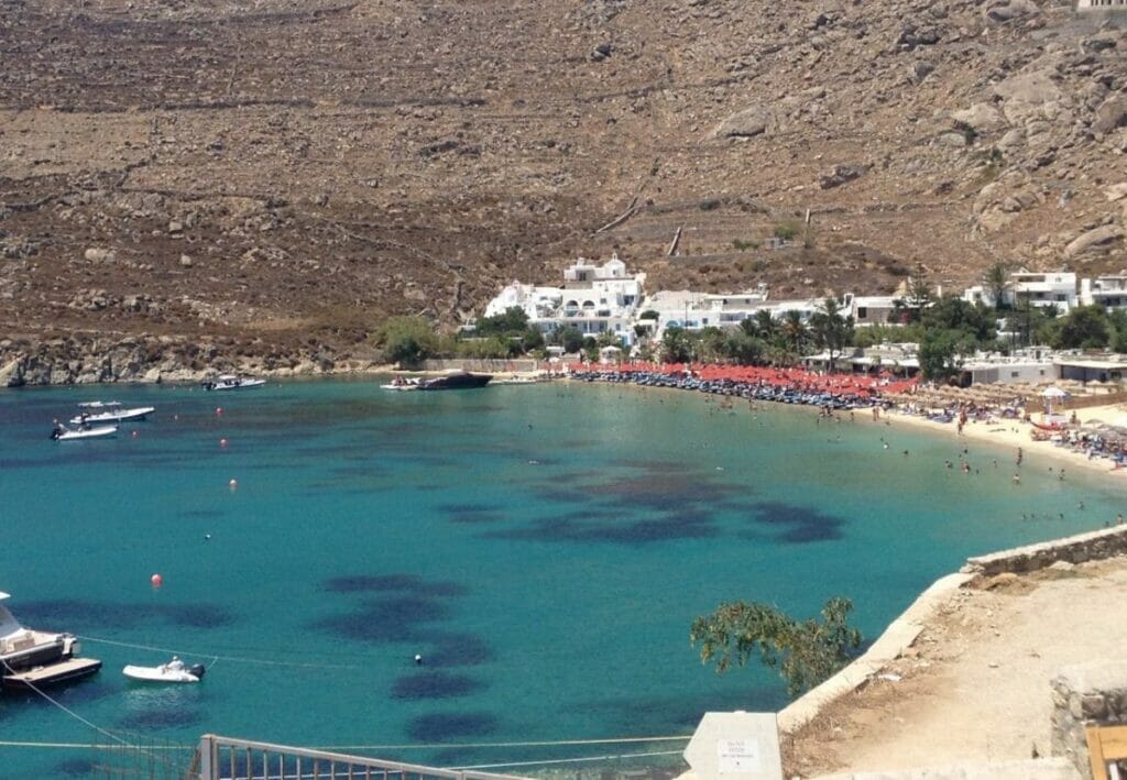 a crystal-clear turquoise water beach surrounded a greyish hill in Mykonos