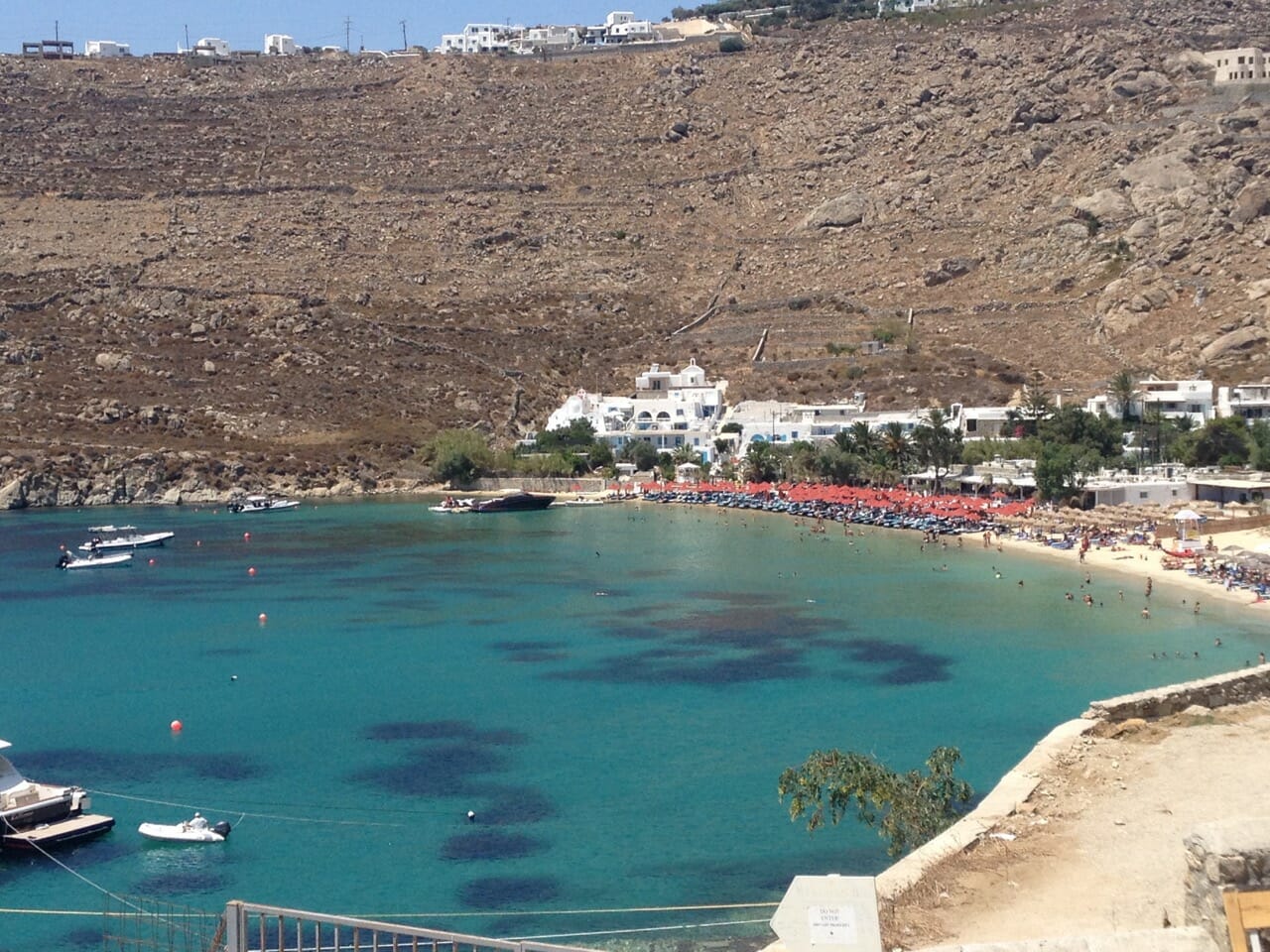 uma praia em Mykonos de água cristalina azul rodeada por uma montanha 