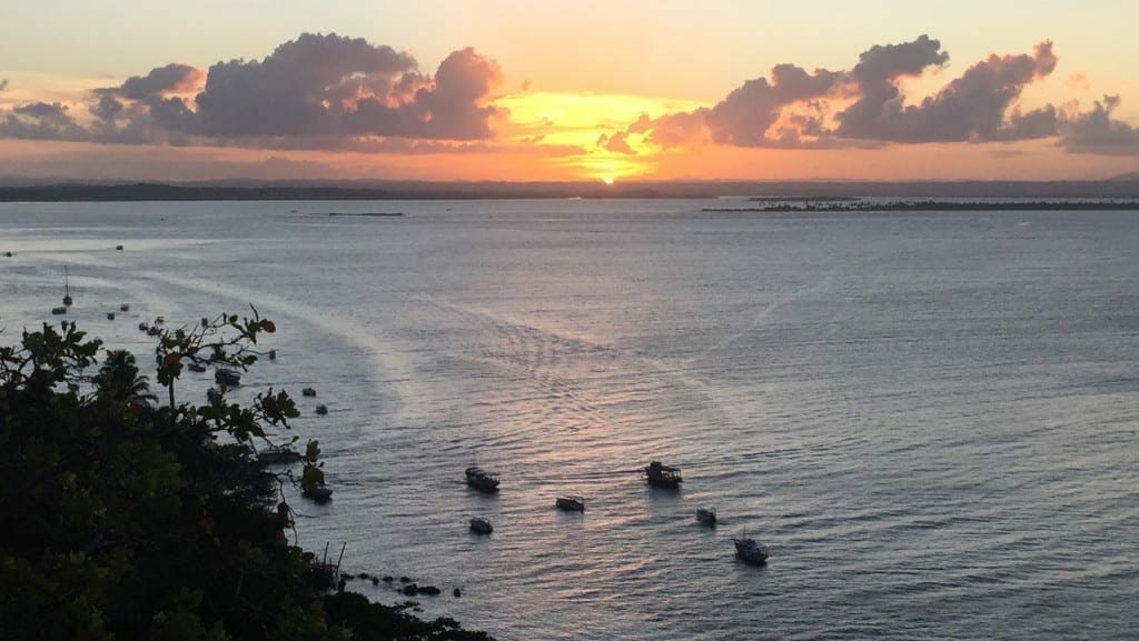 The sun setting in the sea and some boats on the water at Morro de São Paulo, Bahia, Brazil