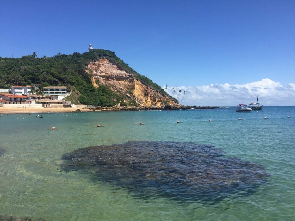 The crystal clear waters of the First Beach, Morro de Sao Paulo, Bahia, Brazil, and a hill covered with vegetation in the background