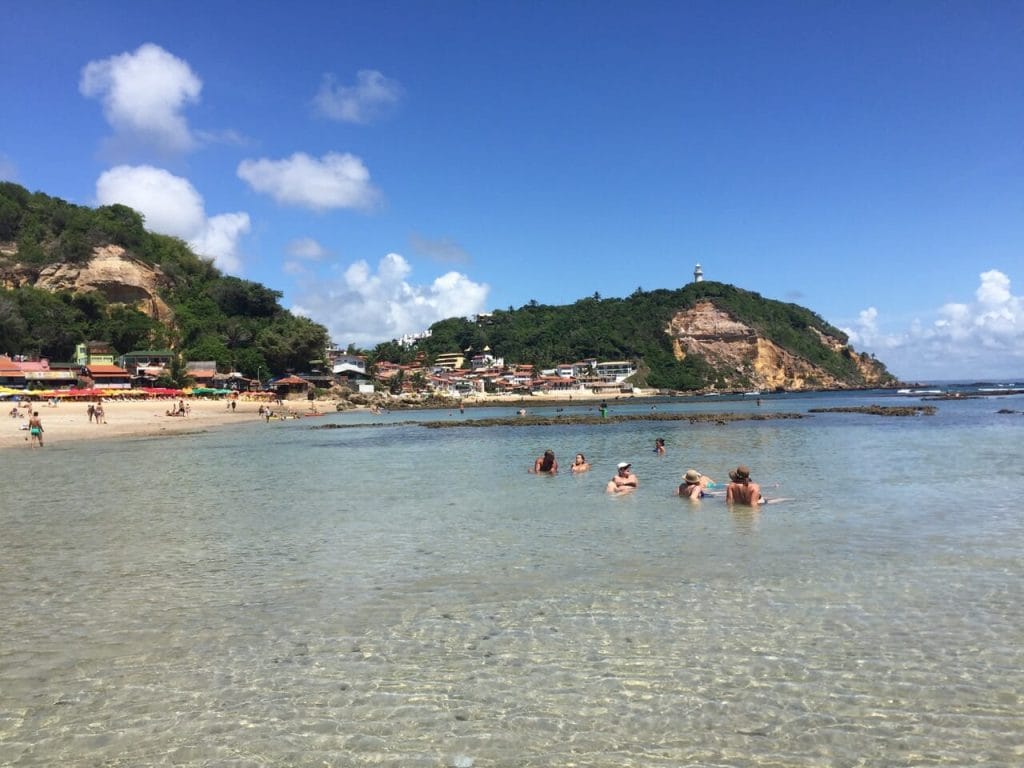 Algunas personas en el agua cristalina de la Segunda Playa, Morro de Sao Paulo, Bahia, que está bordeada por colinas cubiertas de vegetación