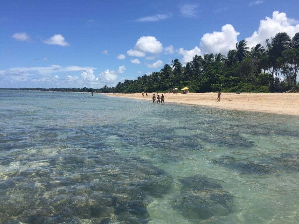 Algumas pessoas andando na Quarta Praia, Morro de São Paulo, que tem água verde cristalina e é cercada por vegetação opulenta