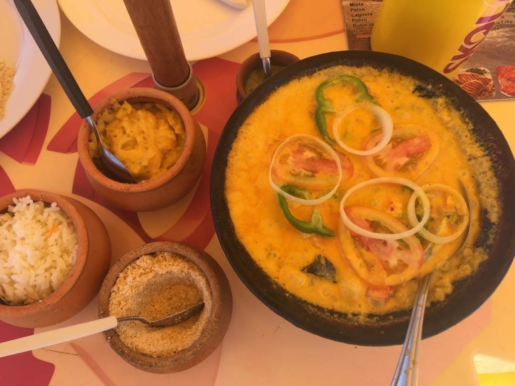 A big bowl with moqueca and three other bowls with side dishes served at Toca do Mar Restaurant in Cova da Onça village, Bahia, Brazil