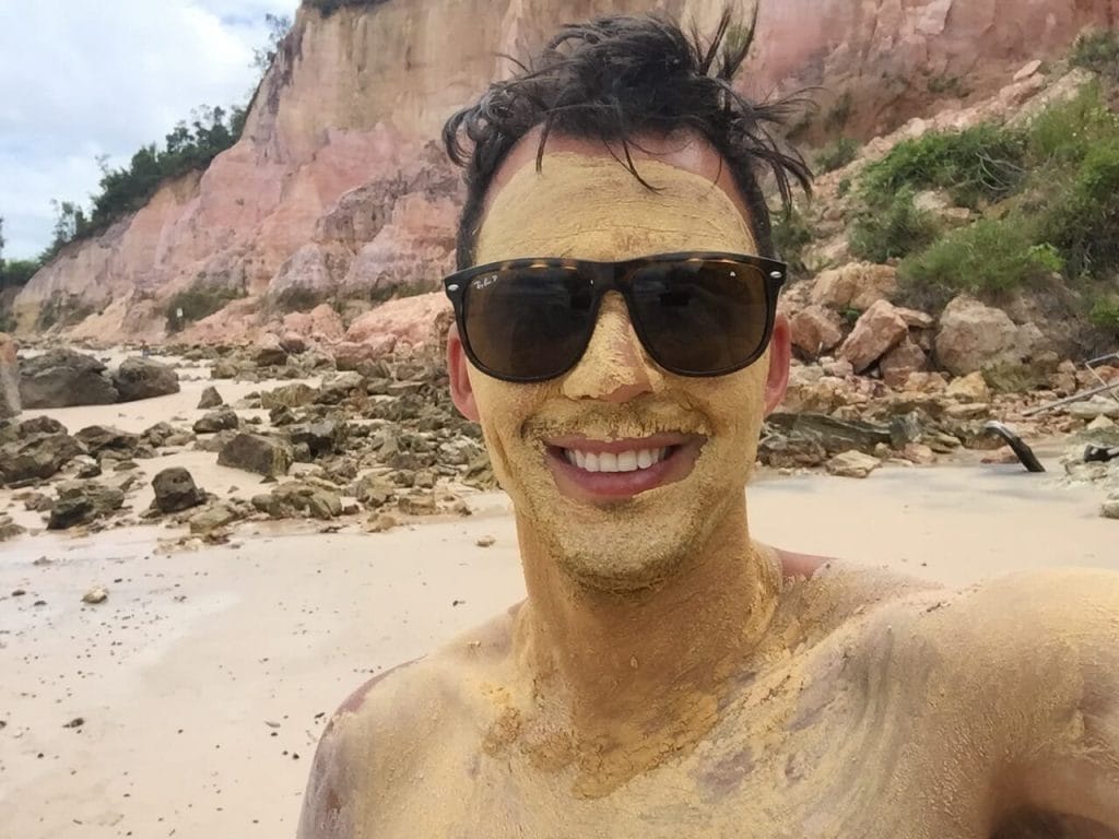 Pericles Rosa is covered with mud and some rocks behind him on Gamboa Beach, Bahia, Brazil