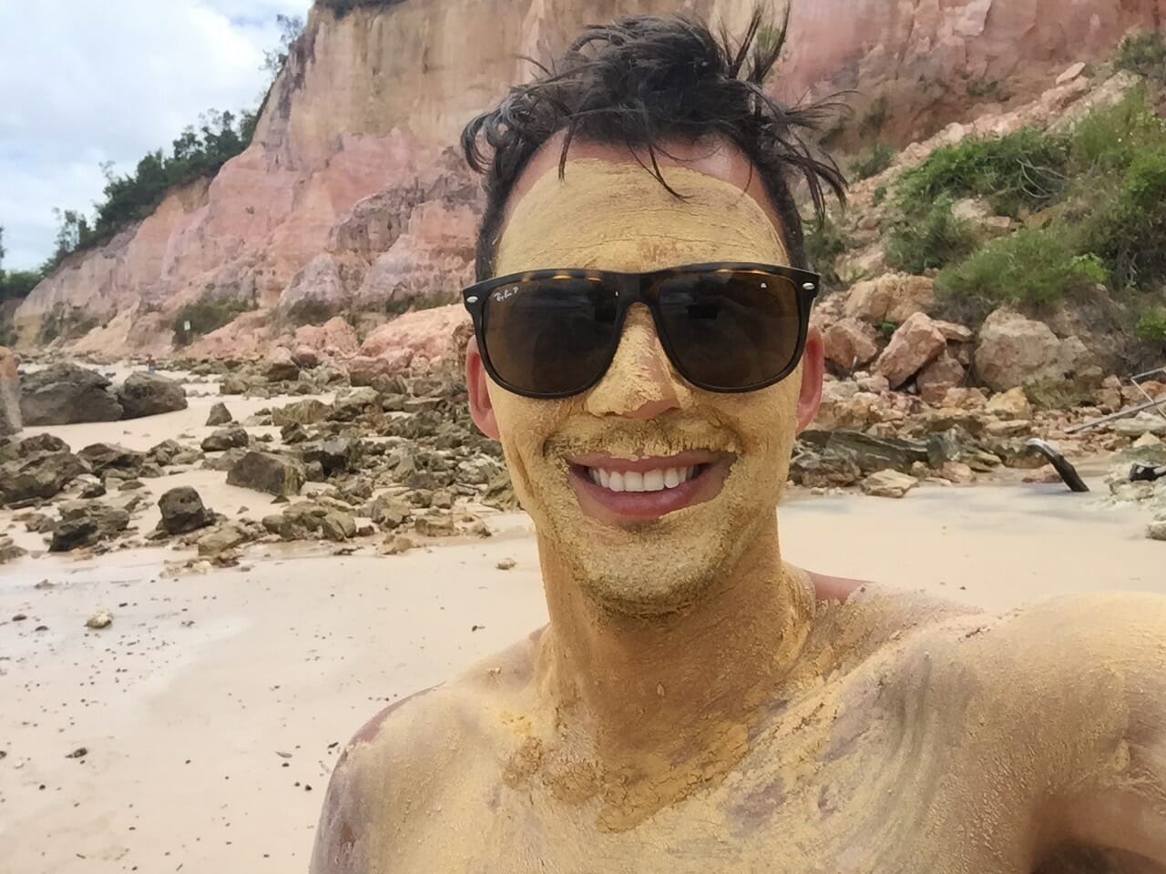 Pericles Rosa cubierto de lodo y algunas rocas detrás de él en la playa de Gamboa, Bahia