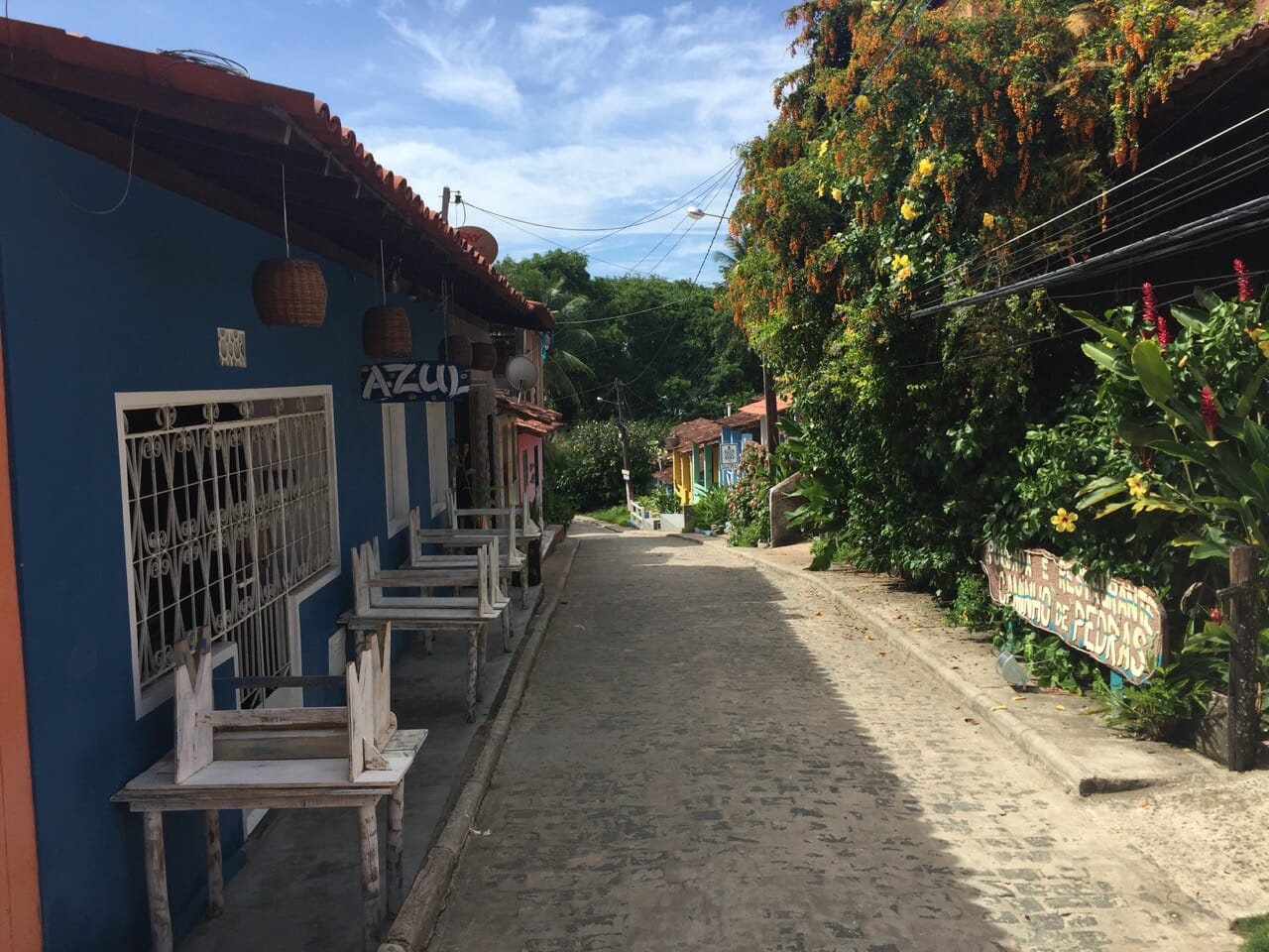 A street in the village of Velha Boipeba wth a house painted in blue with white windows on one side and trees on the other side, Boipeba, Brazil