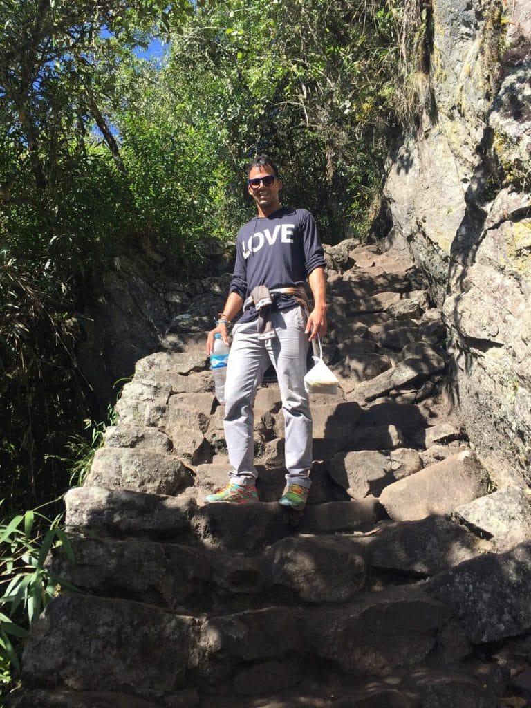 a man wearing a grey trouser and a black long sleeve shirt on the steps of Machu Picchu Mountain hiking trail, Peru