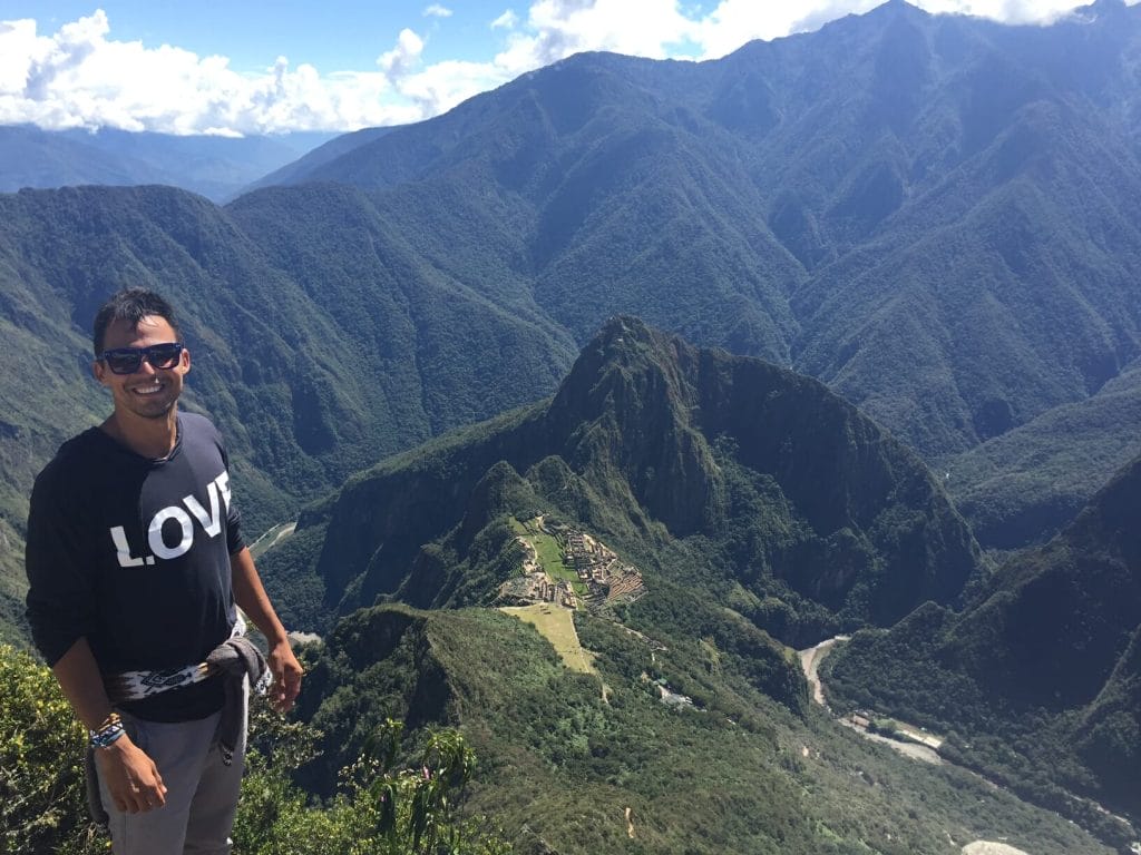 Pericles Rosa no topo da Montaña Machu Picchu com a citadela de Machu Picchu rodeada por montanhas enormes