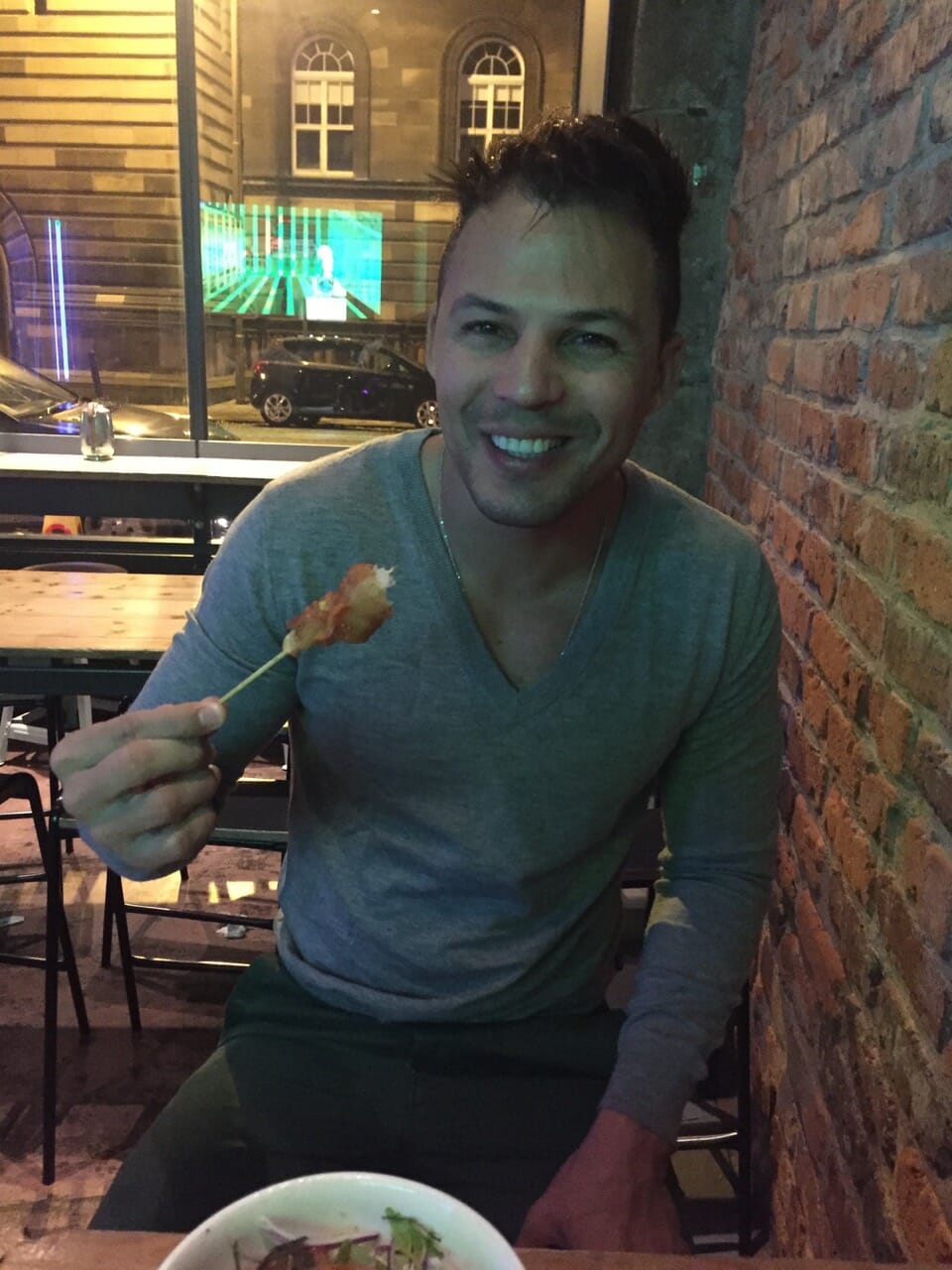 a man wearing a long sleeve grey t-shirt eating a fried chicken skewer at Ting Thai Caravan Restaurant