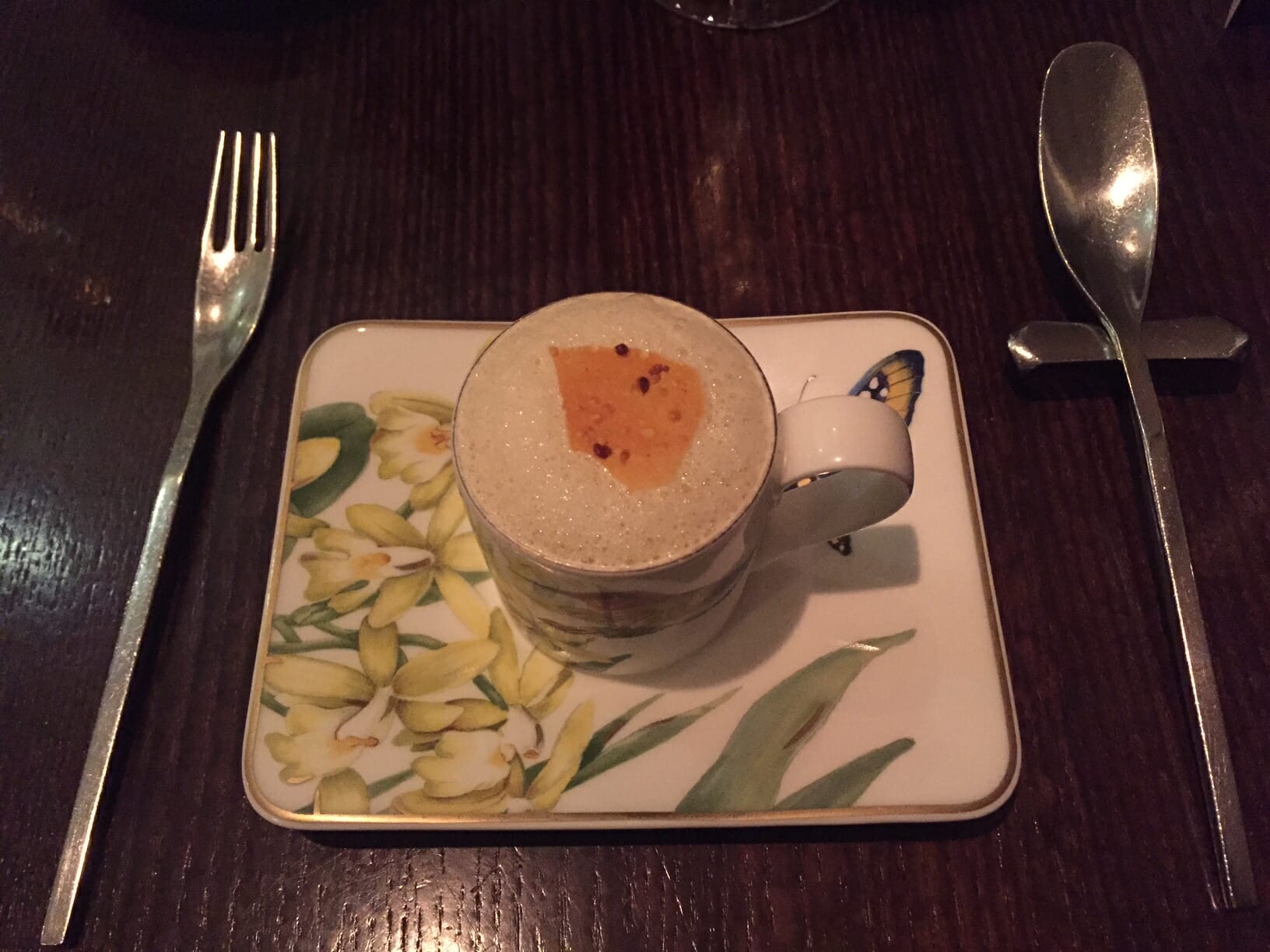 a plate decorated with yellow flowers and a cup with some soup and two silver cutleries