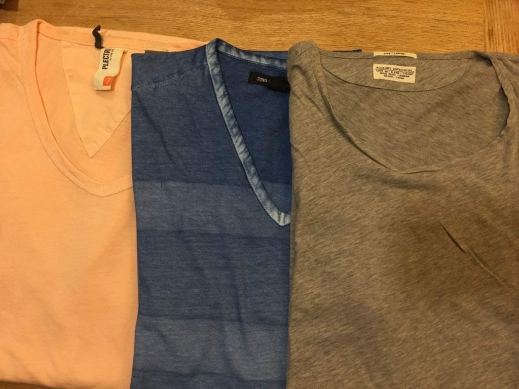 Três camisetas de cores diferentes, dobradas em cima de uma mesa