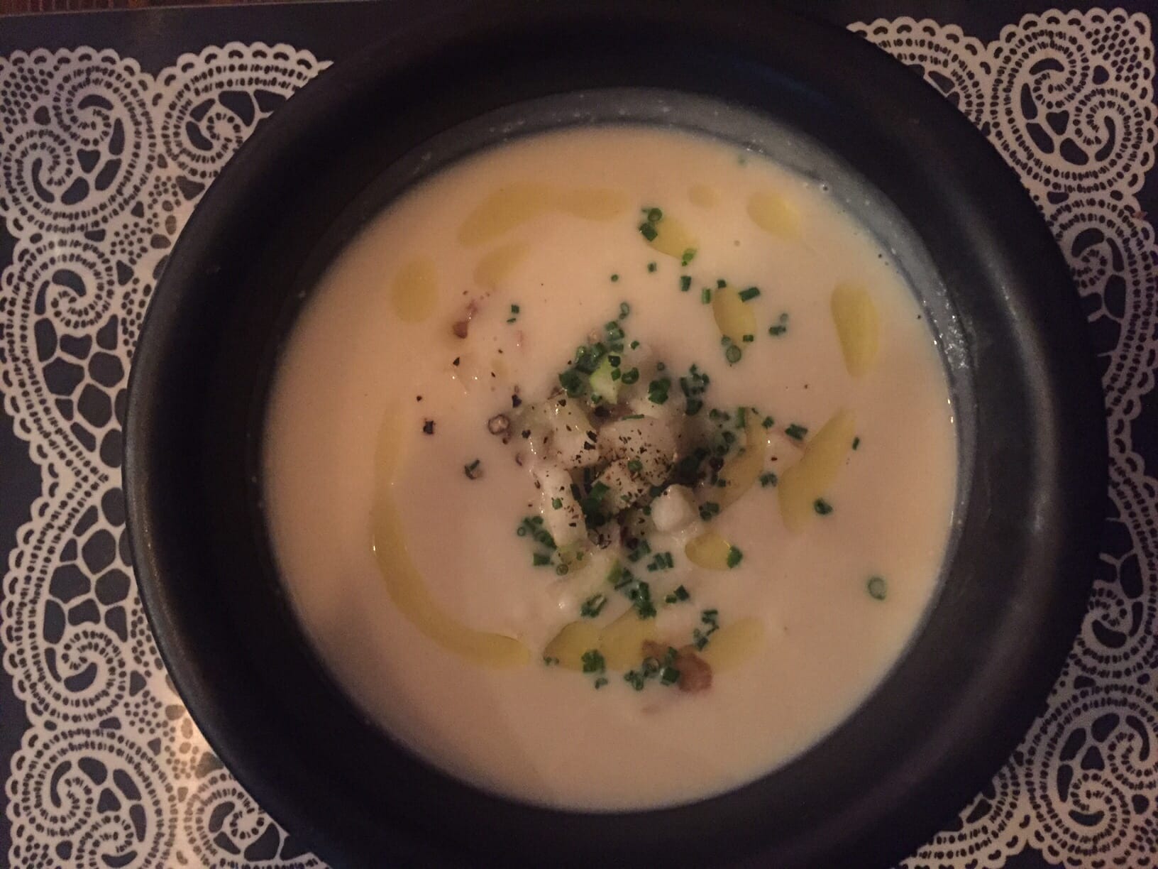 a black bowl with celeriac soup with chestnut and apple on the top of a white place mat