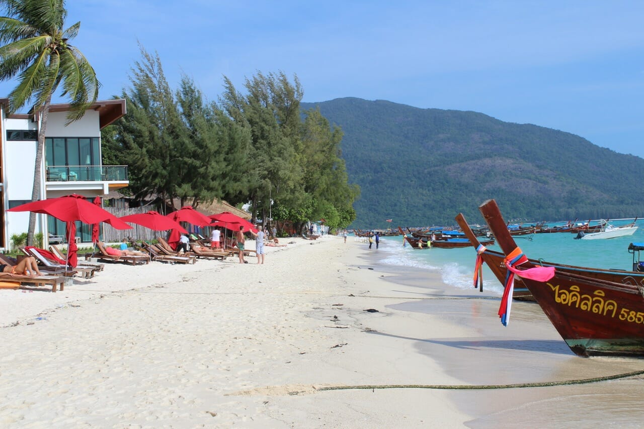 barcos de madera en estilo tailandes, sombrillas de playa rojos y algonos arboles en playa de Sunrise, Koh Lipe, Tailandia