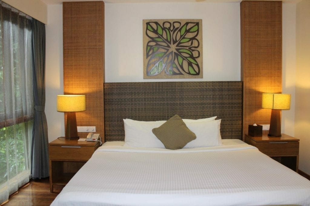 Estudio  bosque tropical del resort Berjaya Langkawi con cama king size, sábanas y almohadas blancas, piso de madera, armazón, muebles, lámparas y ventanas de vidrio