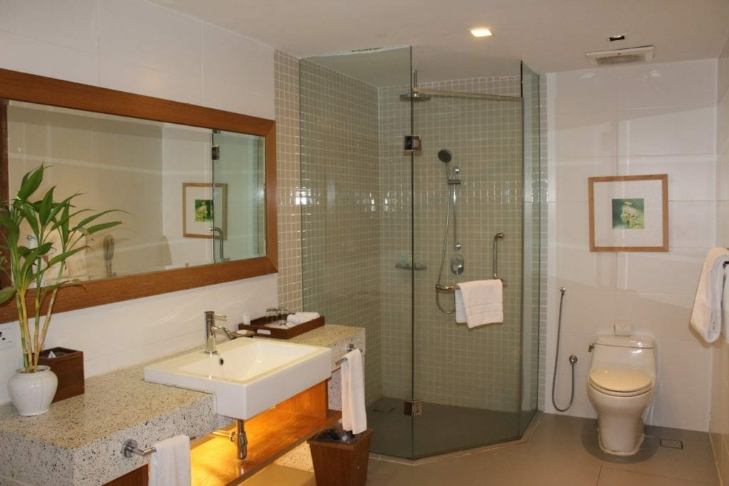 baño con ducha de vidrio, lavabo, plantas, espejos y azulejos blancos