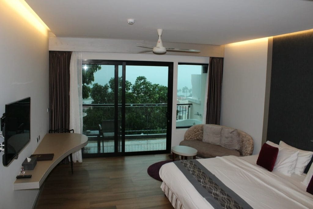 An ocean view room at Avani Cliff Resort, with a king-size bed, couch, TV, balcony and an outdoor bathtub. 