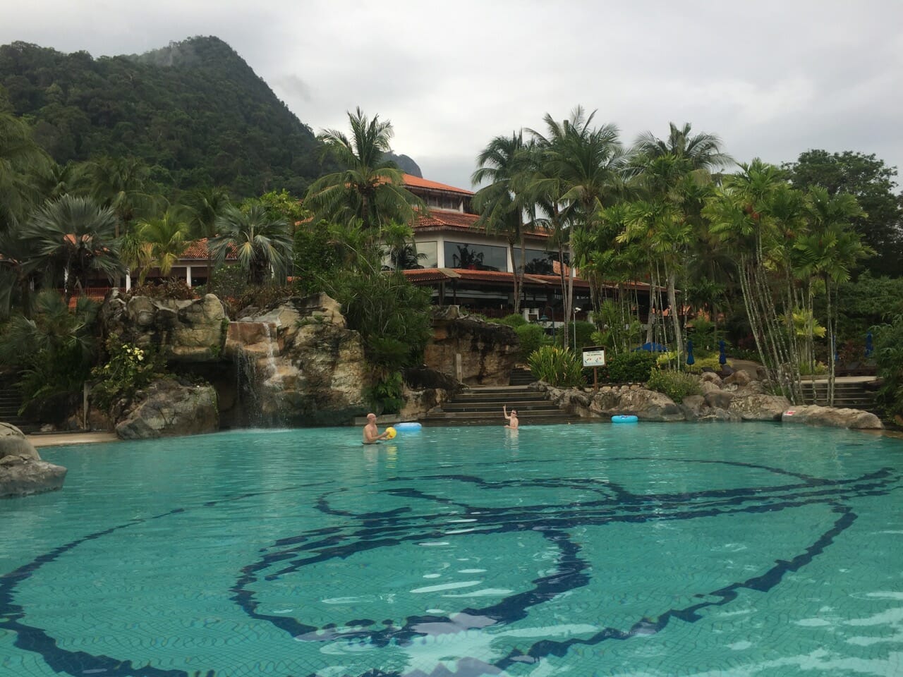 Berjaya Langkawi Resort swimming pool backed up by coconut trees, a building and mountains covered with vegetation