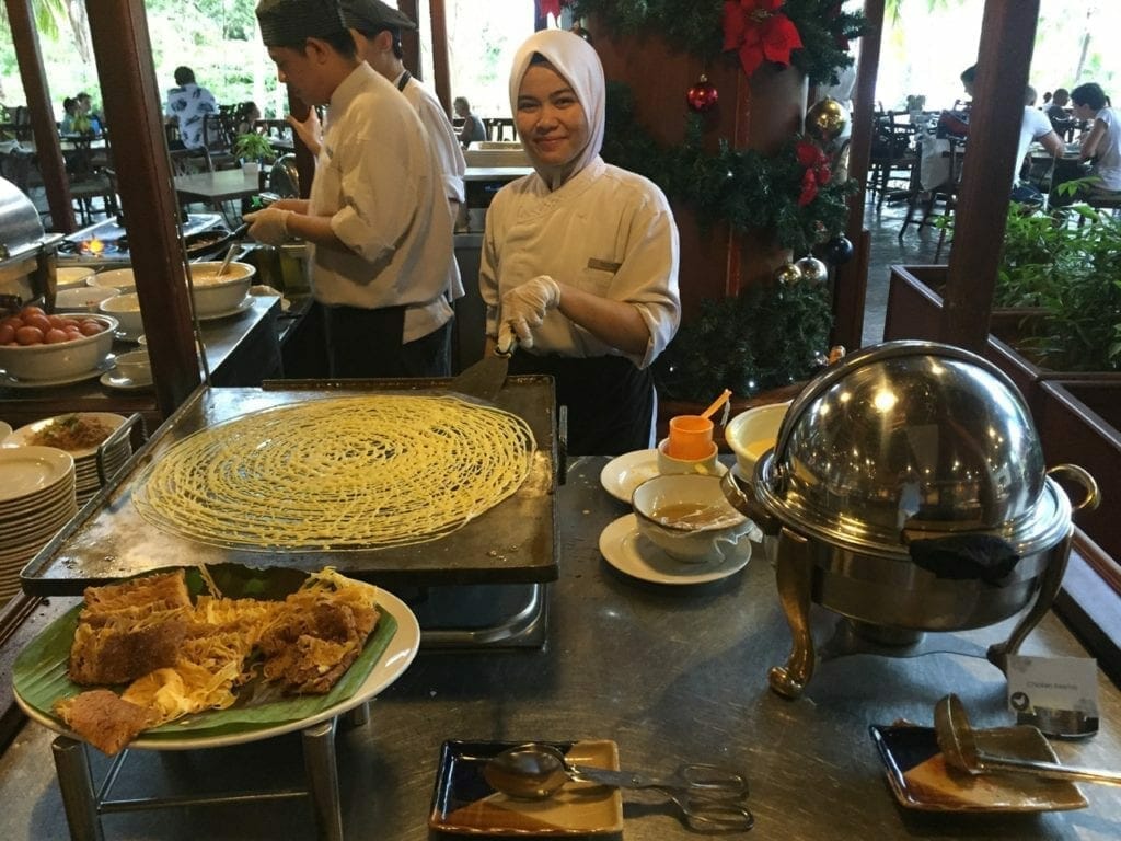 a live cook station with three Malay chefs dressed in white clothes preparing a local dish