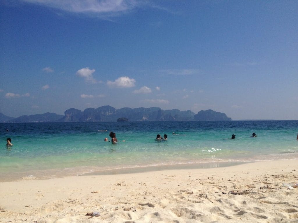 people swimming in the crystalline water of Poda Island, Thailand, and some limestone mountains in the background