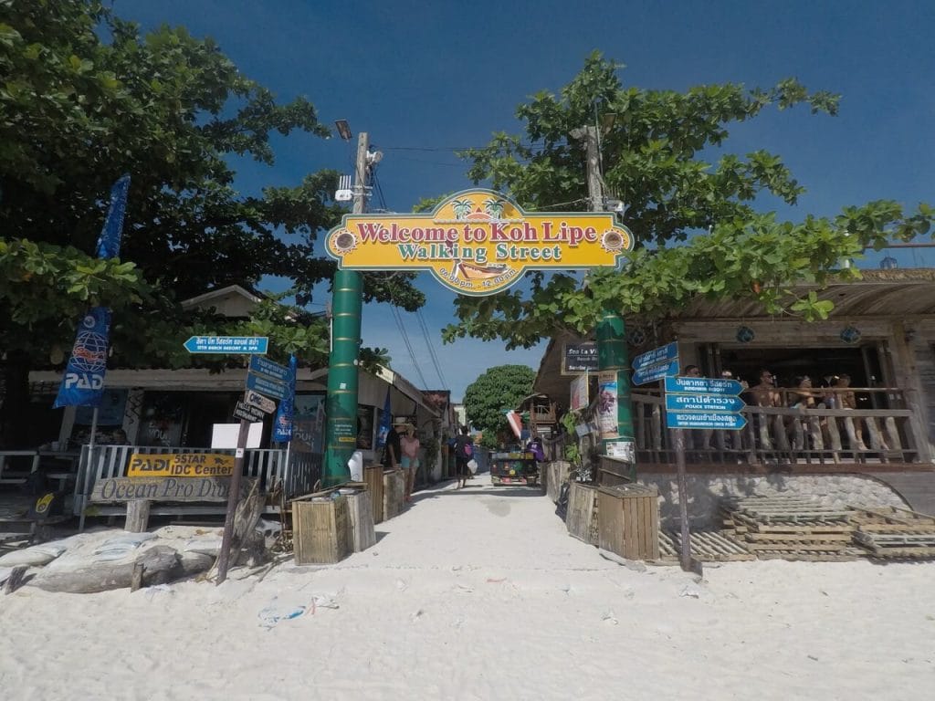 La calle principal de la isla Ko Lipe con arena de la playa, bares de madera y una placa donde se leer Welcome do Koh Lipe - Walking Street