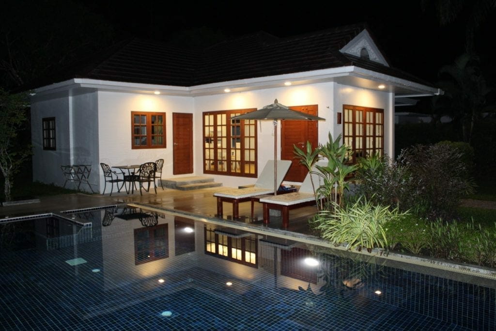 A villa with a swimming pool, garden, lounge chairs, an umbrella, table and chairs