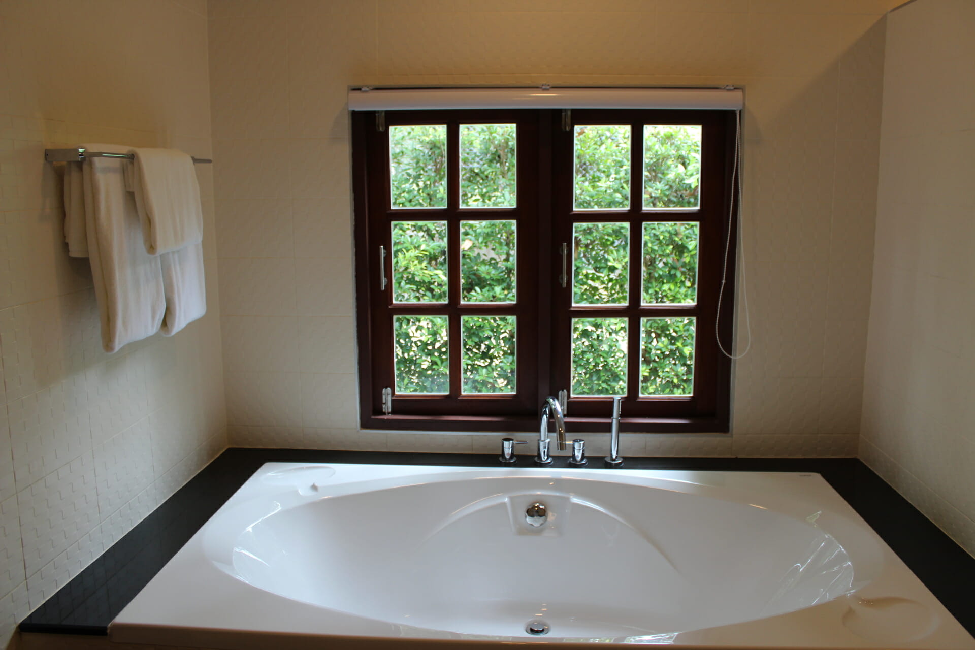 a white bathroom with white towels, white bath tube and windows