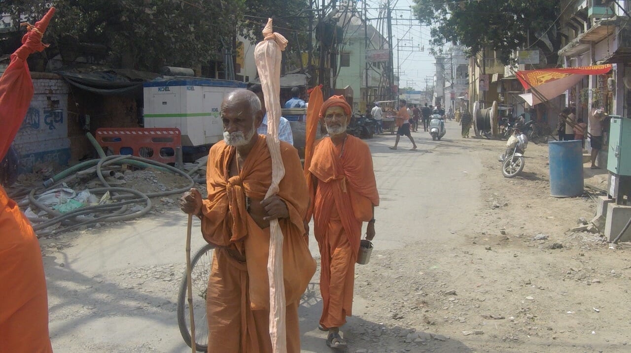dois homens vestindo um manto laranja andando em uma rua de Varanasi