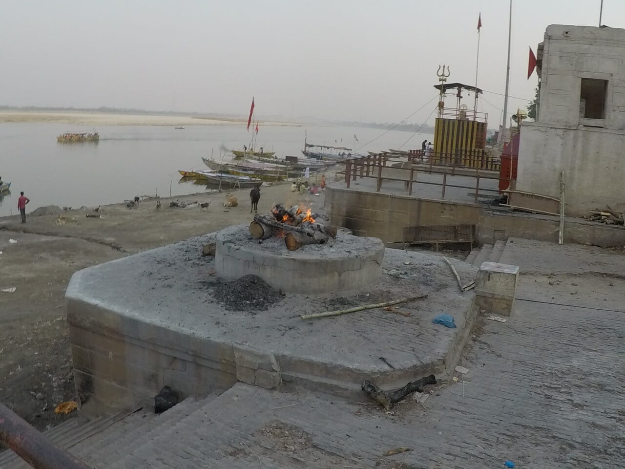 uma plataforma redonda cimentada com algumas madeiras queimando e as águas do rio Ganges