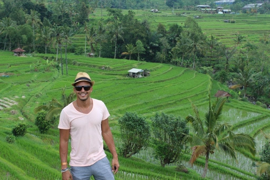 Pericles Rosa wearing a brown hat, sunglasses, salmon t-shirt and grey short at Jatiluwih Rice Terrace, Bali, with  rice fields in the background 