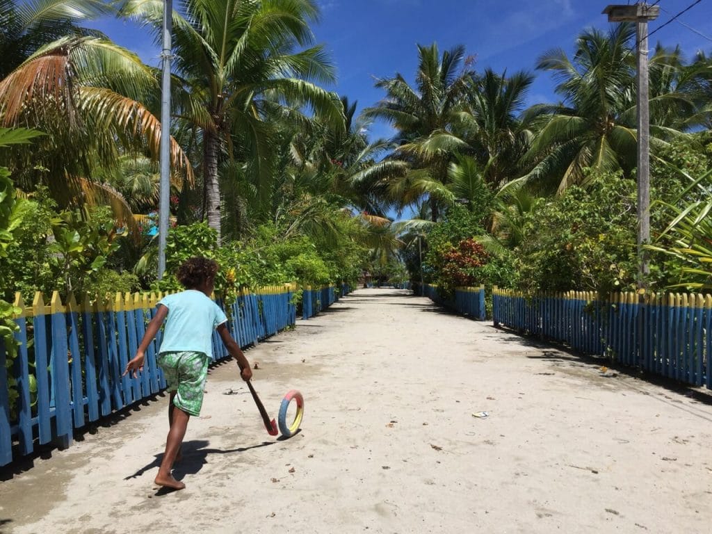 A children playing with a wheel and a piece of wood on a sandy street in Arborek village, Raja Ampat, Indonesia