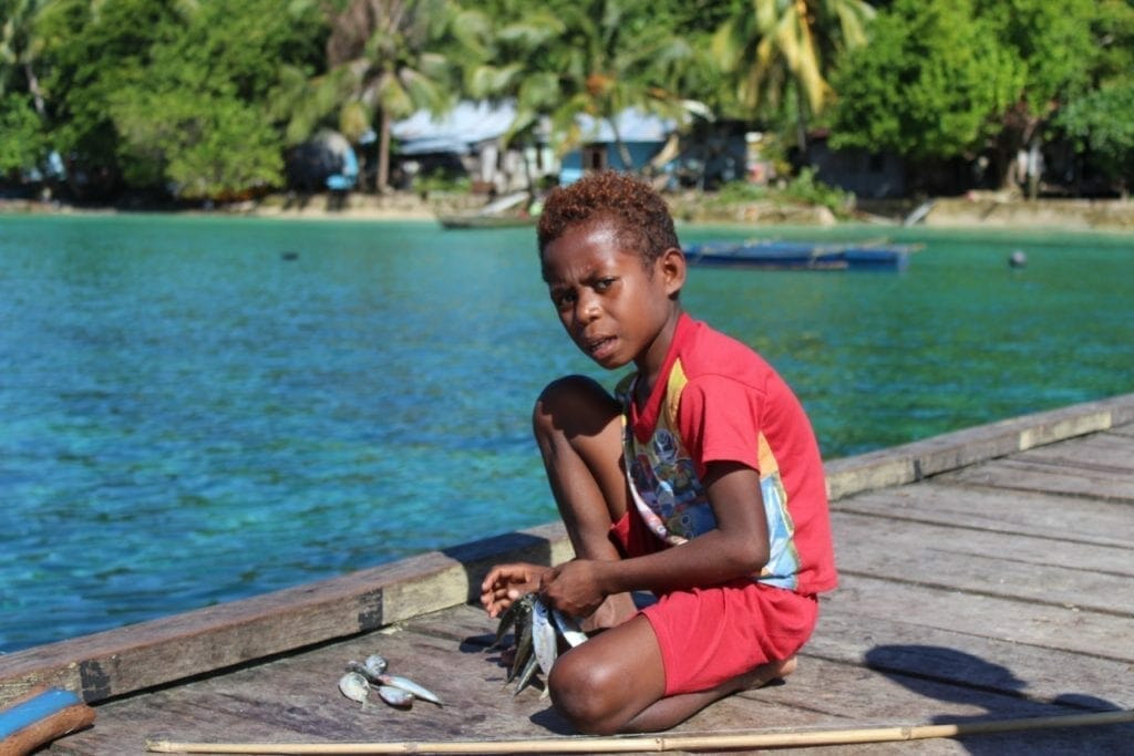 A kid wearing red clothes fishing in Raja Ampat, Indonesia