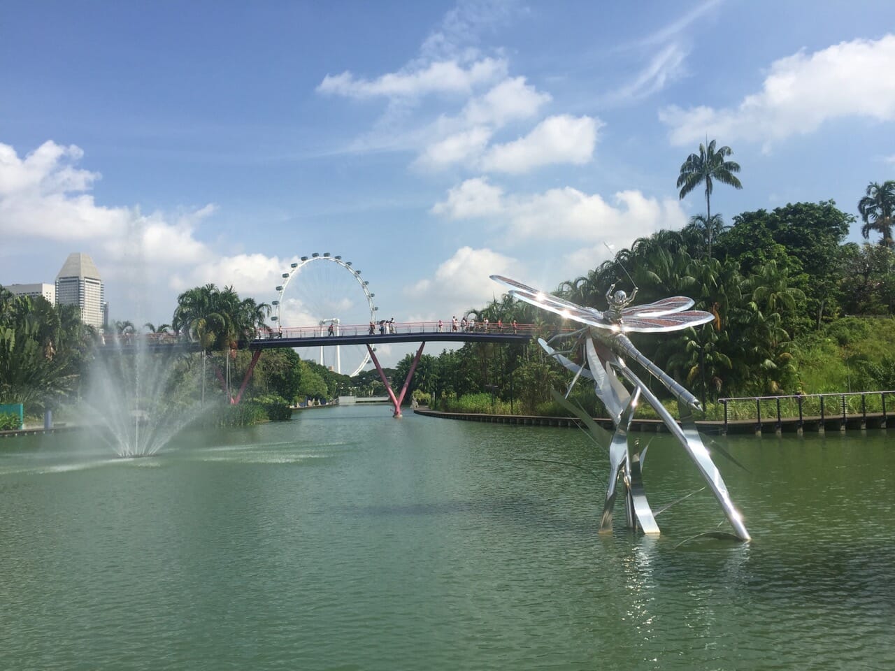 a lake with a silver dragon-fly scuplture, and a bridge in the background