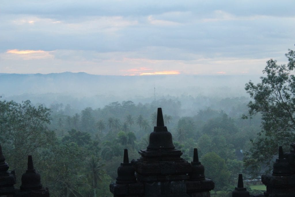 Sol a través de nubes, niebla y árboles en Borobudur