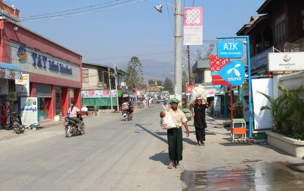 The main street of Nyaung Shwe, Myanmar, with motorbikes, a man and a woman carrying bags