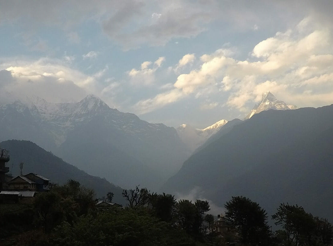 Ghandruk village, Nepal, with a few houses, trees and snow caped mountains in the background 