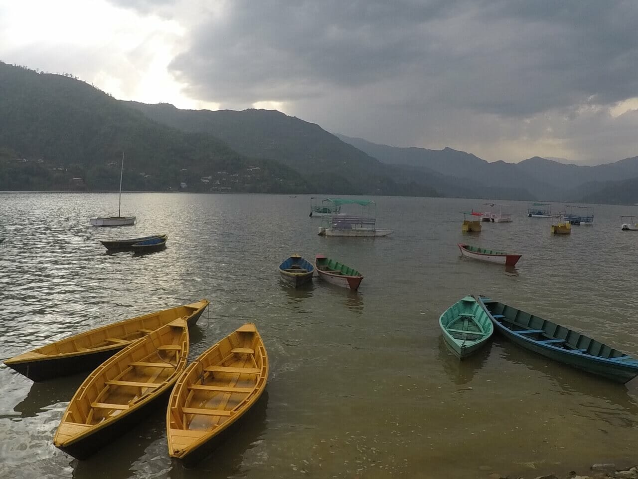 Boats of different colours on a lake in Pokhara, Nepal, and mountains in the background