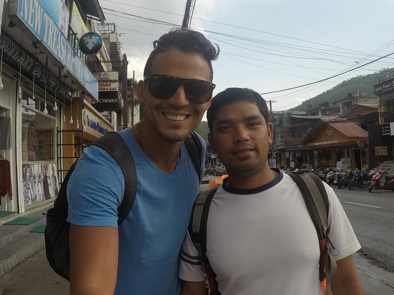 Pericles rosa wearing a blue t-shirt and sunglasses with a local guide on a street in Pokhara, Nepal