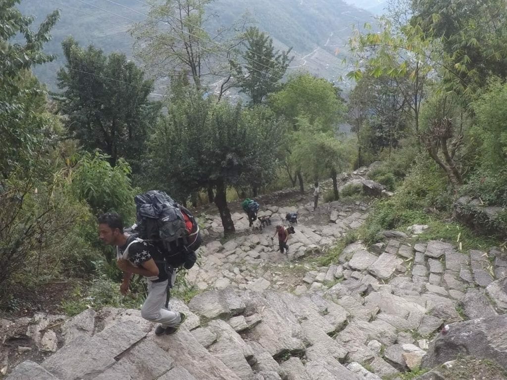 A man carrying a big backpack and climbing up some steps near the village of Ulleri in Nepal