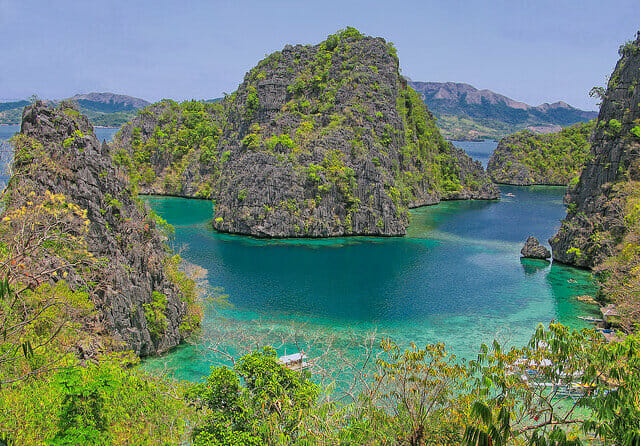 Jagged mountains covered with vegetation and surrounded by crystal-clear turquoise water in Coron, the Philippines.