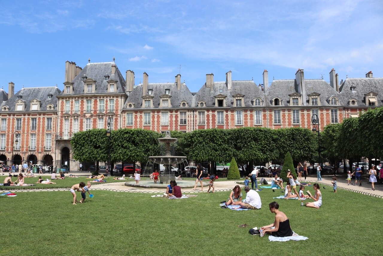 People seating on the grass in the middle of Place des Vosges, originally Place Royale, is the oldest planned square in Paris. Victor Hugo lived here from 1832 to 1848.