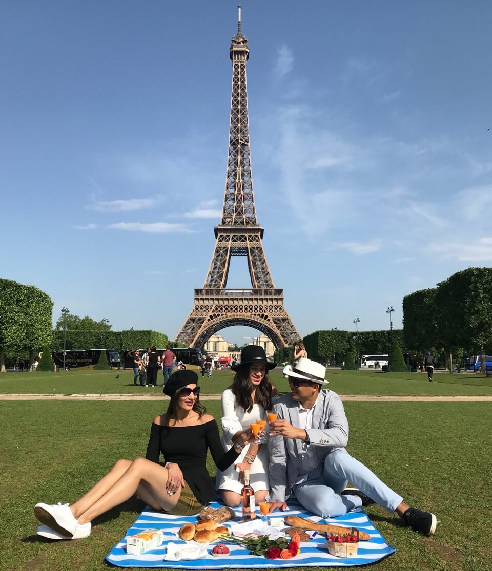 Three people doing a picnic at Parc du Champs-de-Mars, Paris, with the Eiffel Tower in the background.