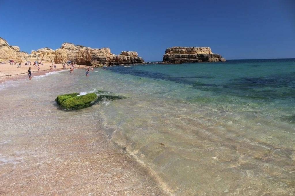 The crystal-clear blue water of Praia do Castelo, Albufeira, Portugal, and some yellow cliffs that surrounds the beach in the background