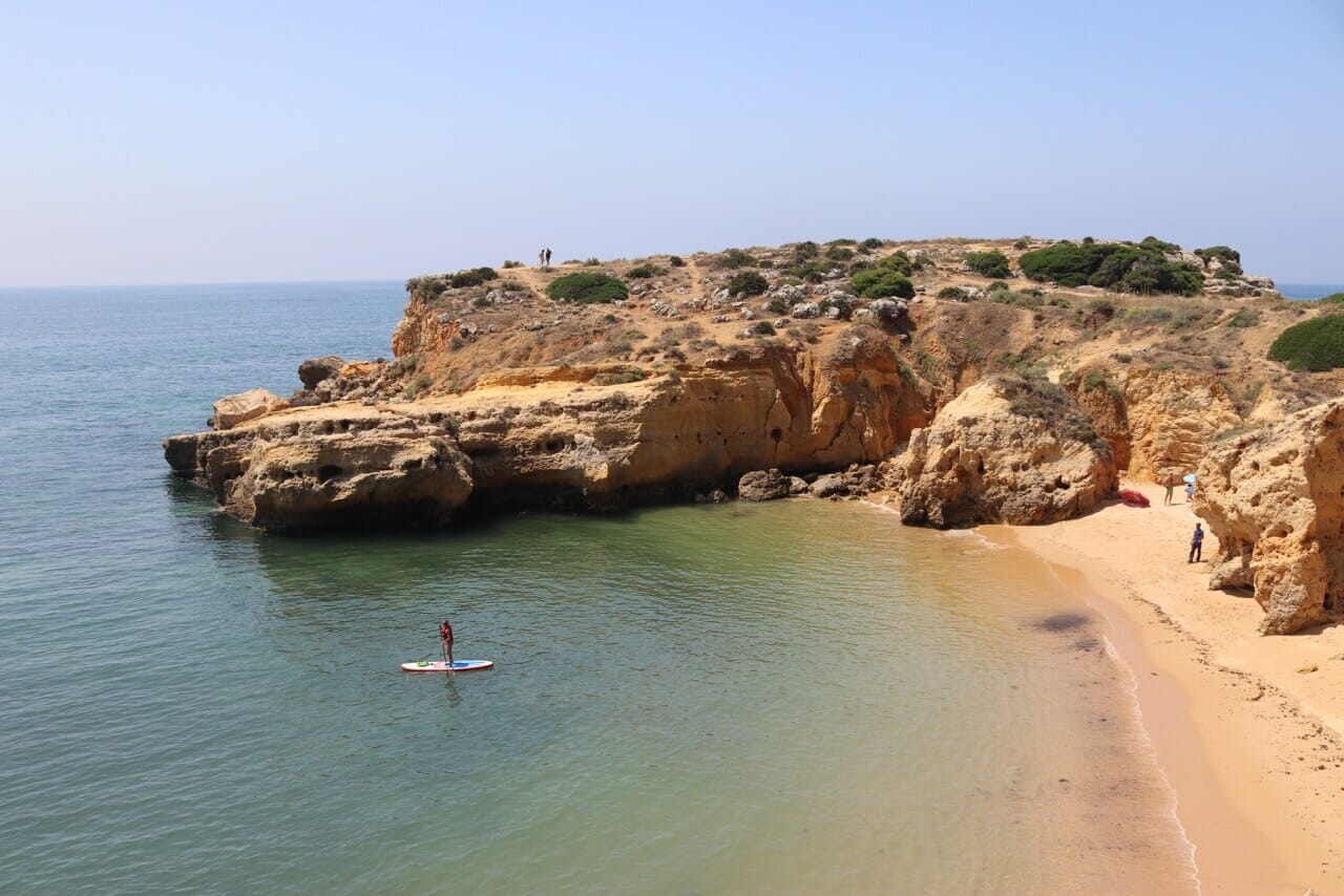 Uma pessoa em um Stand Up Paddle Boarding em uma pequena enseada na Praia dos Arrifes, Albufeira, Portugal