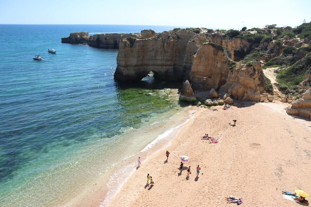 Gente caminando en Praia da Coelha, en Albufeira, que tiene enormes acantilados de piedra caliza ocre y agua azul cristalina